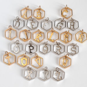 26 hexagon pendants with an initial inside, laid out in alphabetical order showing rows of silver or gold. on a white table