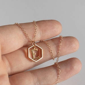 Hand holding a gold hexagon pendant with an initial inside