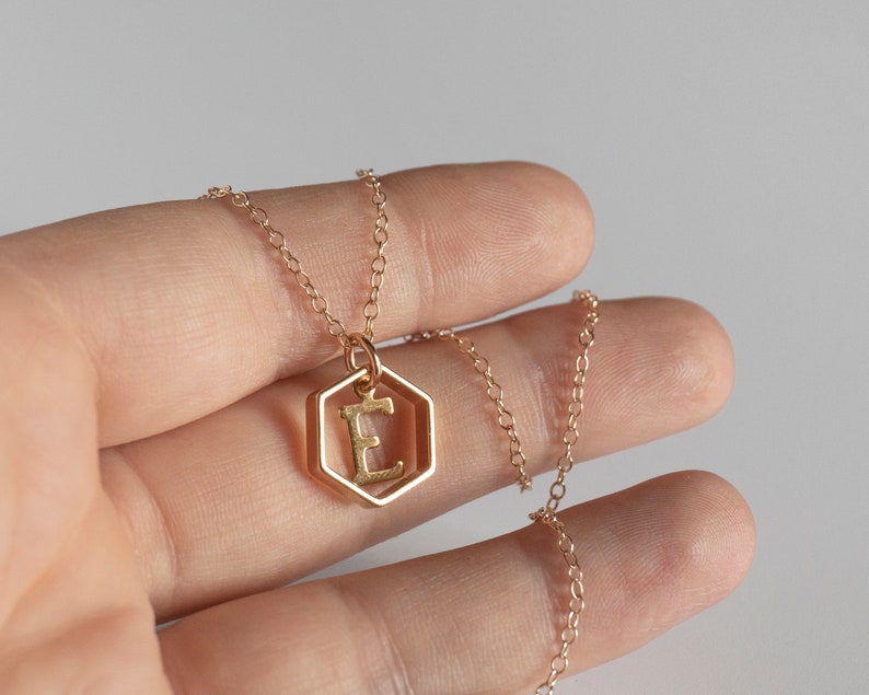 Hand holding a gold hexagon pendant with an initial inside