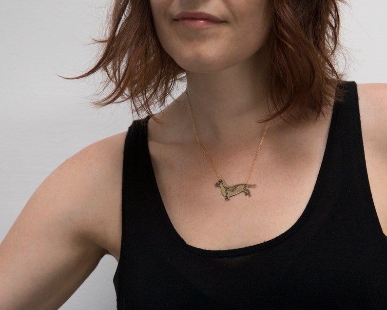 brass dachshund pendant with etched skeleton, worn by a model wearing black tank top with white background.