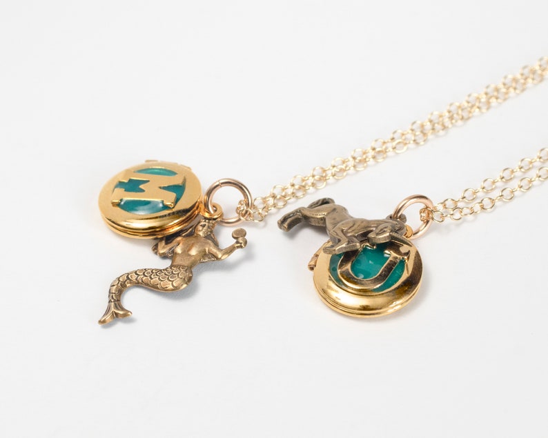 initial lockets with mermaid and unicorn charms, at an angle on white background