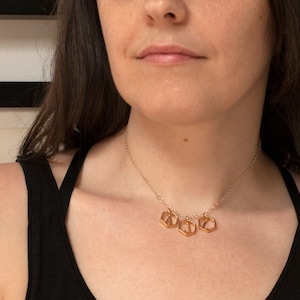 model wearing a gold necklace with 3 initials in hexagons in a row, and a black tank top