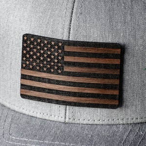 May include: A gray baseball cap with a wooden American flag patch. The flag is made of dark wood with a black and white design.