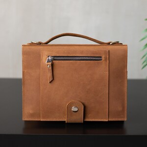 May include: A brown leather briefcase with a zippered pocket and a buckle closure.