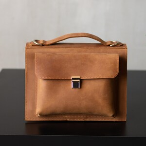 May include: A brown leather briefcase with a flap closure and a silver clasp. The briefcase has a top handle and a shoulder strap.