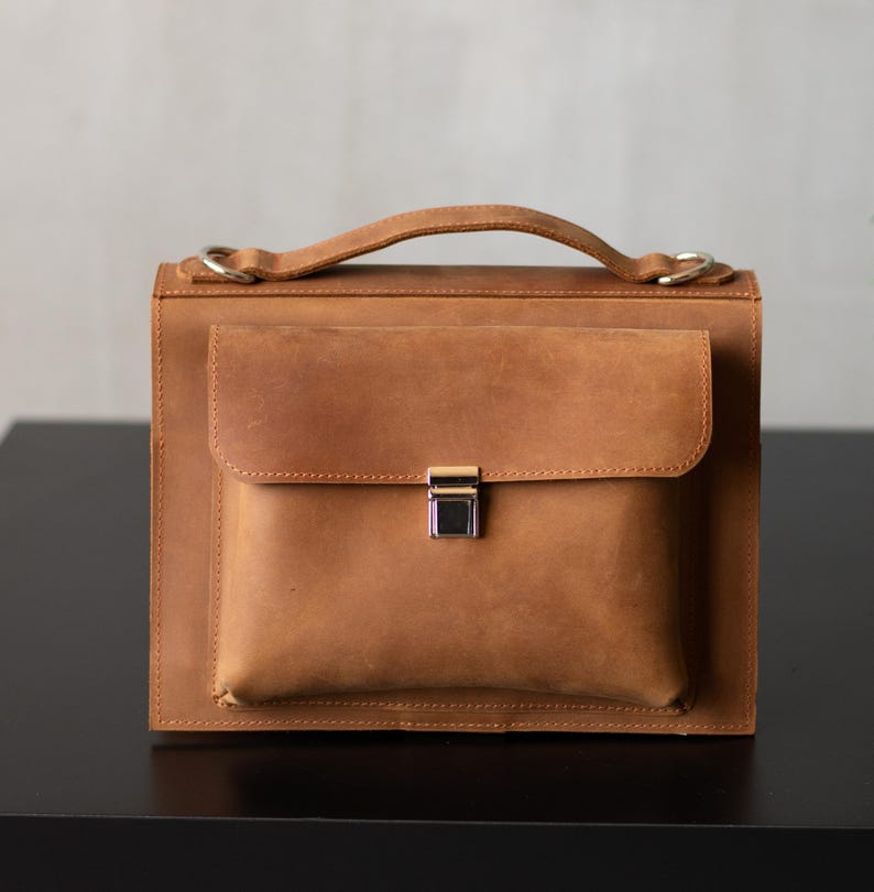 May include: A brown leather briefcase with a flap closure and a silver clasp. The briefcase has a top handle and a shoulder strap.