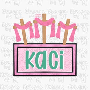 May include: A digital design featuring three wooden crosses with pink fabric draped over them. Below, a pink rectangle with the name "KACI" in teal letters is displayed. The design has a light background.