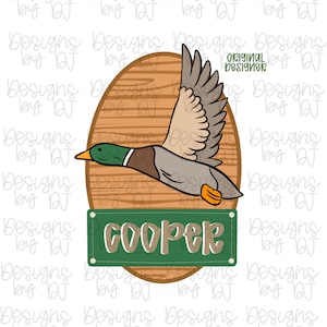 以下が含まれることがあります： 緑、茶色、グレーの羽を持つ飛んでいるアヒルの漫画イラスト。アヒルは木の楕円形の背景に設定されています。アヒルの下には、手書きのスタイルで「COOPER」という名前が入った緑色の長方形があります。