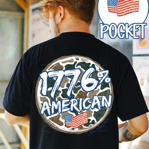 K&ouml;nnte beinhalten: Schwarzes T-Shirt mit einem kreisf&ouml;rmigen Aufdruck auf dem R&uuml;cken. Der Aufdruck zeigt den Text "1776% AMERICAN" in Wei&szlig; und Blau, vor einem Tarnmuster. Enth&auml;lt eine kleine amerikanische Flagge. Das Shirt hat auch einen "USA Edition" Text.