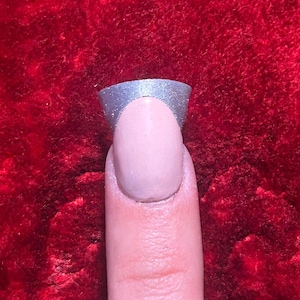 May include: A finger with a light pink nail polish and a silver glitter tip.