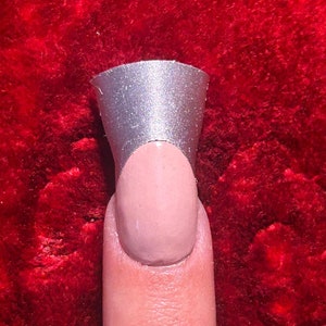 May include: A silver nail tip with a rounded top and a slightly curved edge. The tip is placed on a finger.