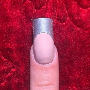May include: A close-up of a finger with a light pink nail polish and a silver tip.