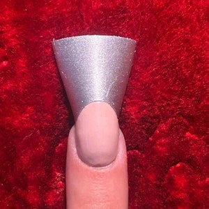 May include: A silver nail tip with a rounded top, placed on a finger.