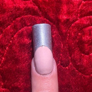 May include: A close-up of a finger with a silver nail polish tip. The nail is painted with a light pink color and the tip is a silver metallic finish.