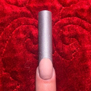 May include: A silver nail polish with a nude base on a finger.