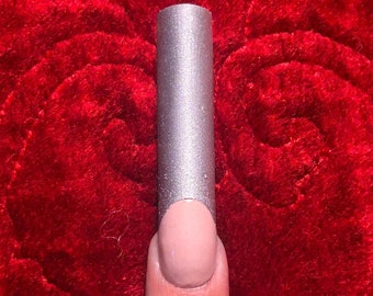 Puede incluir: Un esmalte de uñas plateado con una base nude en un dedo.