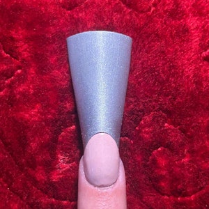 May include: A silver nail tip is placed on a finger with a light pink nail polish.