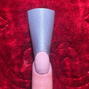 May include: A silver nail guide for applying nail polish. The guide is shaped like a cone and is placed on a finger.
