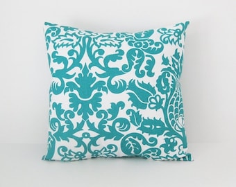 May include: A square throw pillow featuring a vibrant teal damask pattern printed on a crisp white background. The intricate, symmetrical floral and scrollwork design covers the entire front surface of the pillow, creating a bold contrast.