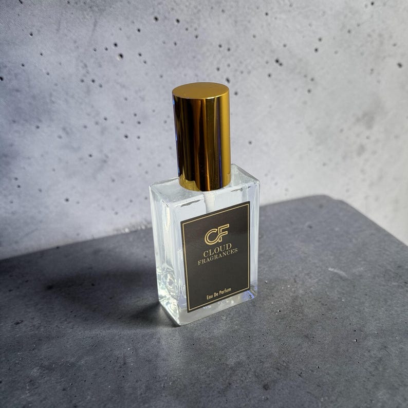 Pu&ograve; includere: Un flacone di profumo in vetro trasparente con tappo dorato. Il flacone &egrave; rettangolare e ha un'etichetta nera con la scritta "CF CLOUD FRAGRANCES Eau De Parfum". &Egrave; appoggiato su una superficie grigia.