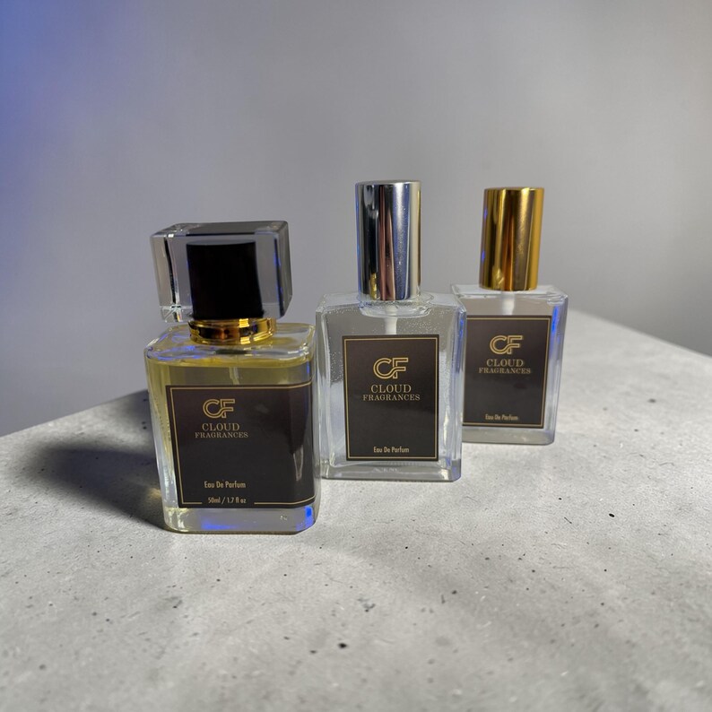 Pu&ograve; includere: Tre flaconi di profumo con vetro trasparente e tappi metallici. Ogni flacone ha un'etichetta marrone scuro con la scritta "CF CLOUD FRAGRANCES". I flaconi sono riempiti con un liquido color ambra chiaro. Il flacone anteriore ha un tappo nero ed &egrave; etichettato "Eau De Parfum 50ml / 1.7 fl oz".