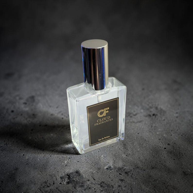 Pu&ograve; includere: Un flacone di profumo trasparente e rettangolare con tappo argentato. Il flacone ha un'etichetta nera con testo dorato che recita "CF CLOUD FRAGRANCES Eau de Parfum". Il flacone &egrave; su una superficie grigio scuro.