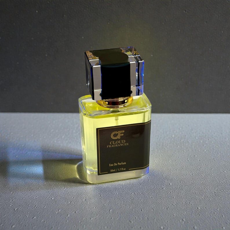 Pu&ograve; includere: Un flacone di profumo quadrato con un corpo in vetro trasparente e un liquido giallo all'interno. Il flacone ha un'etichetta nera con scritte dorate e un tappo decorativo con una parte superiore nera e una base trasparente sfaccettata. L'etichetta recita "CF Cloud Fragrances Eau de Parfum 50ml / 1.7 fl oz."