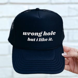 May include: Black trucker hat with a white embroidered design that says "wrong hole but i like it."