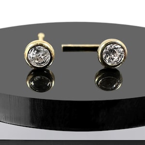 Op de afbeelding: Een paar gouden oorbelletjes met kleine ronde, heldere edelstenen.