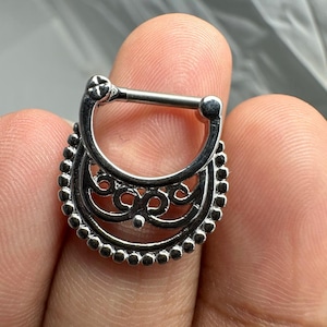 Peut inclure: Bijou de corps en argent avec un design décoratif et orné. Le bijou est en forme de croissant de lune avec un bord perlé.