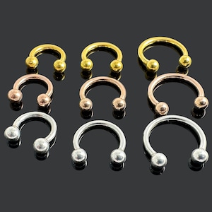 Könnte beinhalten: Ein Set aus neun hufeisenförmigen Körperschmuckstücken in Gold, Roségold und Silber. Der Schmuck ist aus Metall und hat abgerundete Enden.