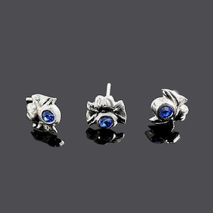 Puede incluir: Tres pendientes de plata con detalles de piedras preciosas azules. Cada pendiente tiene un diseño floral detallado.