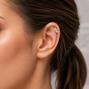 Könnte beinhalten: Ein Ohrstecker für den Knorpelbereich, bestehend aus drei klaren, marquise-geschliffenen Steinen in blattartiger Anordnung. Das Schmuckstück verfügt über eine silberfarbene Metallfassung und einen sicheren Verschlussmechanismus.