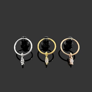 May include: Three hoop earrings with a dangling marquise-shaped clear stone. The hoops are available in silver, gold, and rose gold.