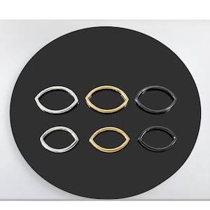 Könnte beinhalten: Sechs verschiedene farbige, metallene, augenförmige Creolen. Die Ohrringe sind in zwei Reihen zu je drei angeordnet. Die Ohrringe sind silber, gold und schwarz.