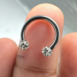 May include: A silver horseshoe-shaped ring with clear crystal embellishments on each end.