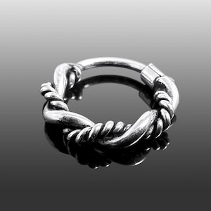 May include: A silver-colored hinged hoop earring with a twisted rope design. The earring is circular, with a clasp closure. The twisted rope design wraps around the hoop, creating a textured appearance. The earring is displayed on a reflective surface.