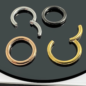 Könnte beinhalten: Vier verschiedene Arten von nahtlosen Ringen für Körperpiercings. Die Ringe sind aus verschiedenen Metallen, darunter Silber, Gold und Schwarz. Die Ringe sind alle geschlossen und haben eine glatte Oberfläche.