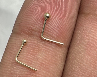 May include: Two gold nose rings with a small ball at the end. The rings are bent at a 90-degree angle.