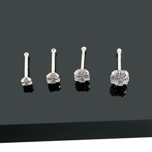 May include: Four silver nose studs with clear, round-cut cubic zirconia stones. The studs are arranged in a row, showcasing varying stone sizes. Each stud has a straight post and a small, round ball at the end.