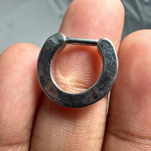 May include: A silver hinged segment ring, a type of body jewelry, is shown on a finger.