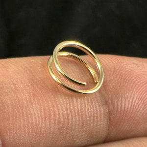 Könnte beinhalten: Ein kleiner, goldfarbener Doppelreifen-Ohrring. Der Ohrring ist eine durchgehende Schlaufe mit einer zweiten, kleineren Schlaufe. Der Ohrring wird vor einem neutralen Hintergrund gezeigt.