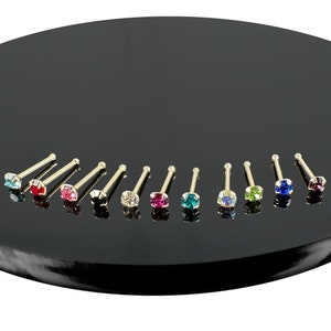 May include: A selection of nose studs with gold-coloured posts and a variety of square-cut gemstones. Gemstones include blue, red, pink, clear, purple, teal, light blue, green, dark blue, and magenta.