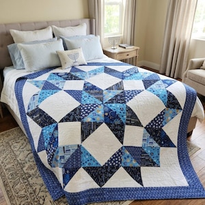 May include: A bed quilt featuring a large central star pattern in shades of navy blue, royal blue, and light blue, contrasted with white fabric sections. The quilt has a dark blue patterned border and is displayed on a bed with blue and white pillows.