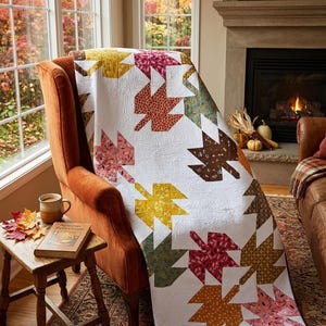 May include: A white quilt featuring a repeating pattern of maple leaves in various autumn colors including red, orange, yellow, brown, and green. The fabric has a quilted texture with swirling patterns throughout the white background.