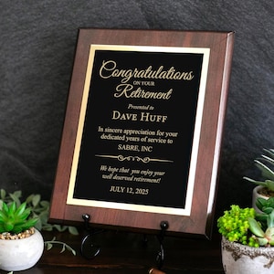 Puede incluir: Una placa rectangular de madera con acabado marrón oscuro y una placa central negra con texto grabado en oro que dice Congratulations on your Retirement, Presented to DAVE HUFF, In sincere appreciation for your dedicated years of service to SABRE, INC, We hope that you enjoy your well deserved retirement! JULY 12, 2025.