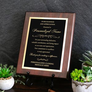 Könnte beinhalten: Eine rechteckige Auszeichnungstafel aus Holz mit dunkelbraunem Finish und einer schwarzen Metallplatte. Die Platte trägt goldenen Text: IN RECOGNITION AND APPRECIATION, Presented to Personalized Name, For your outstanding dedication, valuable contributions, and lasting impact on our team and organization. Your commitment to excellence is truly appreciated. Thank you for making a difference. PERSONALIZED CLOSING MESSAGE HERE.