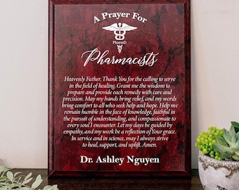 May include: A rectangular wall plaque with a dark red faux marble finish featuring white text that reads A Prayer For Pharmacists, a caduceus symbol, a prayer, and the name Dr. Ashley Nguyen printed in a clear, legible white font.