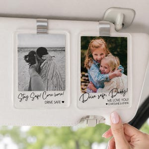 May include: Two rectangular clear acrylic car visor clips featuring custom photo prints. The left clip shows a black and white beach photo with the text Stay Safe! Come home! DRIVE SAFE. The right clip shows a color photo of two children with the text Drive safe, Daddy! WE LOVE YOU! CAROLINE & EMMA.