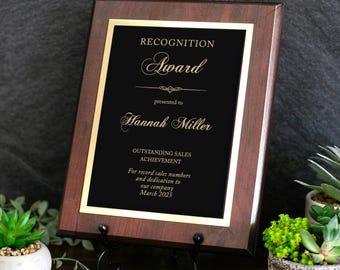May include: A rectangular wooden award plaque with a dark brown finish and a black center plate. The plate features gold text reading RECOGNITION Award presented to Hannah Miller OUTSTANDING SALES ACHIEVEMENT For record sales numbers and dedication to our company March 2025.